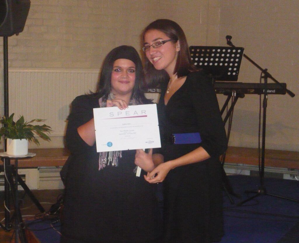 Young person holding certificate with keyboard and music stand in background